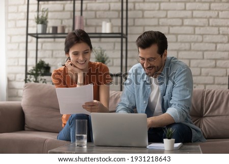 Good news by mail. Happy married couple sit at home office by paperwork manage family business accounting. Glad young spouses read financial report get profit tax refund check information using laptop Royalty-Free Stock Photo #1931218643