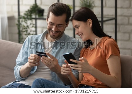 We can well afford to buy it. Happy loving married couple make payment purchase at ecommerce web site online using phone app credit card. Smiling young spouses engaged in shopping at internet pay safe Royalty-Free Stock Photo #1931219915