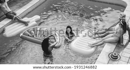 Happy multiracial friends having fun inside swimming pool during summer holidays - Black and white editing - Focus on faces