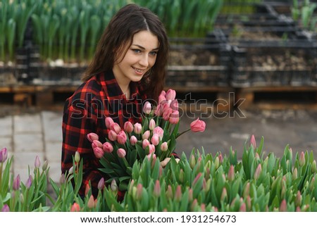 Young beautiful woman greenhouse worker holds a blooming tulips in her hands and smiles.