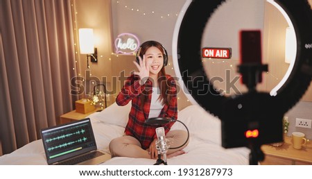 asian woman with microphone has live stream and singing through smartphone in bedroom at home