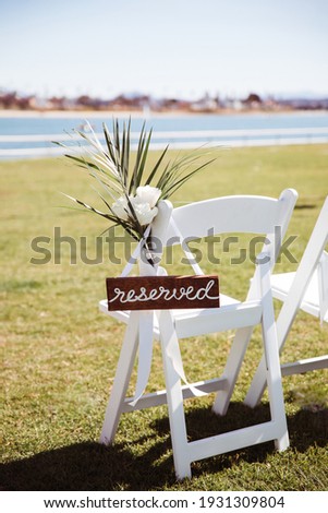 White wooden chair with rustic Reserved sign on green lawn . Outdoor wedding ceremony