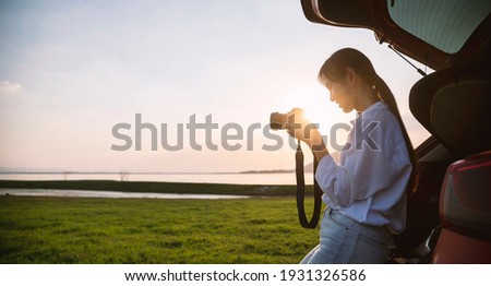 Tourist asian woman sitting at car trunk looking photo on camera that has taken a picture of the view landscape.