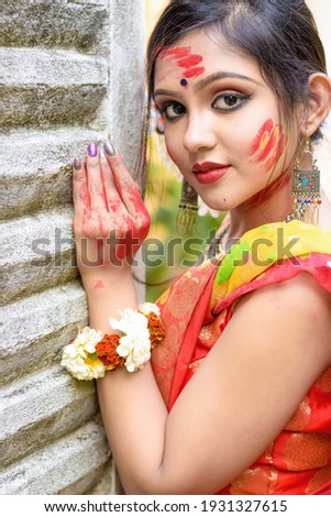Portrait of pretty young indian girl wearing traditional saree and jewellery, playing with colors on the festival of colours called Holi, popular hindu festival celebrated across india.