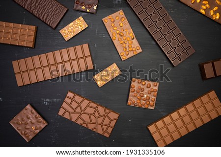 different sweet, delicate chocolate bars lie creatively on a black wooden background