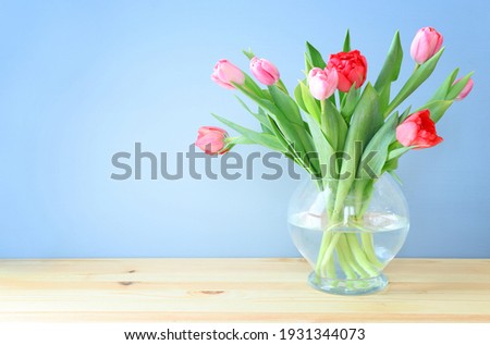 spring bouquet of red and pink tulips flowers in the glass vase over wooden table