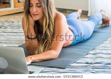 Young sporty woman working out at home, teenager doing fitness exercises on living room floor for buttocks body shaping using online personal training program with laptop, doing yoga pilates indoors
