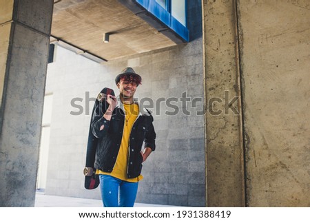 Young student walk with skate board and smile in the city background - concept of teenager boy people enjoy the outdoor leisure activity in town - handsome caucasian male portrait