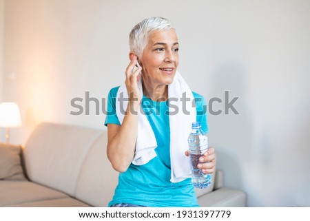 Senior woman with headphones while resting after workout. Athletic mature woman resting after a good workout session