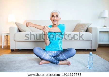 Senior woman doing warmup workout at home. Fitness woman doing stretch exercise stretching her arms - tricep and shoulders stretch . Elderly woman living an active lifestyle.