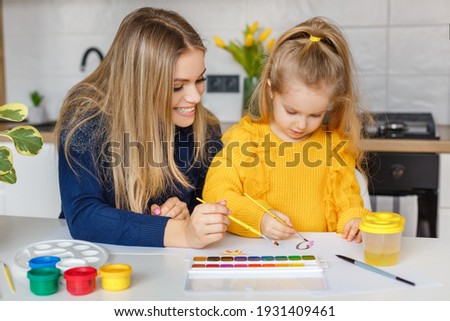 Mother and daughter painting at home. Cute little kid in yellow sweater having fun with parent and paints. Concept of early childhood education, hobby, talent, preschool leisure and parenting Royalty-Free Stock Photo #1931409461