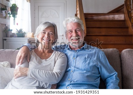 Portrait of happy middle aged retired family couple relaxing on cozy sofa at home. Smiling sincere loving mature senior homeowners looking at camera, posing for photo, showing love and care indoors.