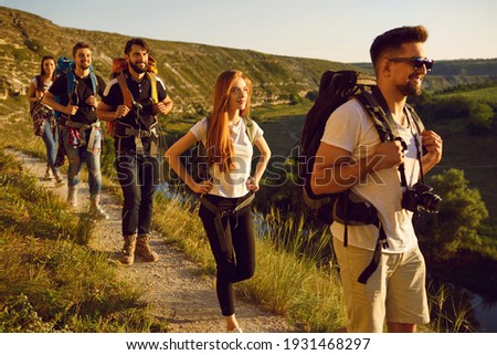 Group of men and women walk in a row along the trail during a walking tour of the mountains. Adventure, travel, tourism, hike and people concept. Camping season. Royalty-Free Stock Photo #1931468297
