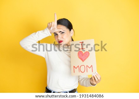 Beautiful woman celebrating mothers day holding poster love mom message making fun of people with fingers on forehead doing loser gesture mocking and insulting.