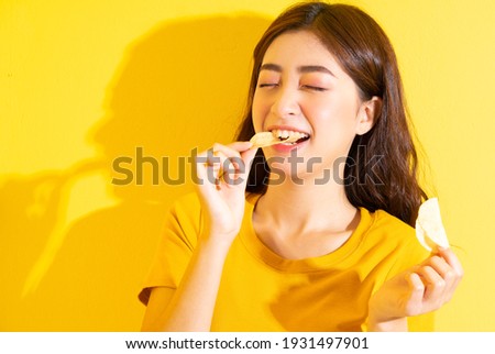 Young Asian girl eating snack on yellow background Royalty-Free Stock Photo #1931497901