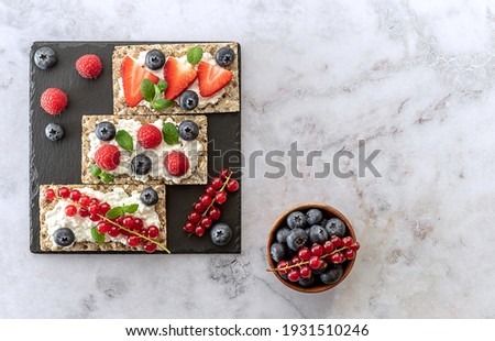 Fresh summer fruits healthy snack of rye oats crisps bread with ripe berry, mint leaves, and cottage cheese, top view, copy space. Royalty-Free Stock Photo #1931510246