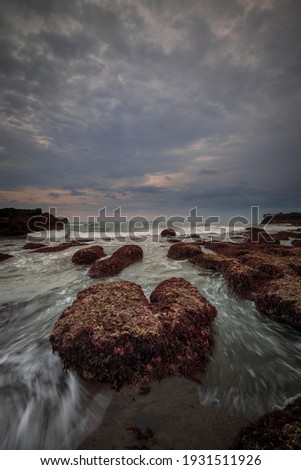 Amazing seascape for background. Beach with rocks and stones. Low tide. Motion water. Cloudy sky. Slow shutter speed. Soft focus. Copy space. Vertical layout. Mengening beach, Bali, Indonesia