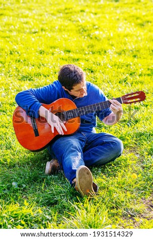 attractive man playing Spanish guitar sitting in a park in spring.