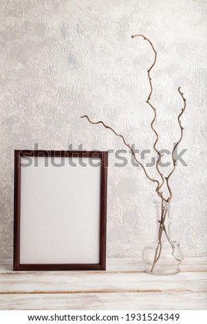 Brown wooden frame mockup with dried wine branch in glass on gray concrete background. Blank, vertical orientation, still life, copy space.