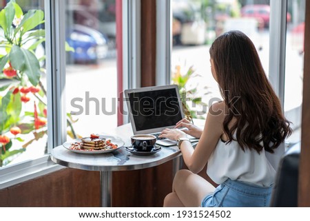 An Asian woman working with a laptop, eating Cape Strawberry and Cappuccino in a coffee shop.