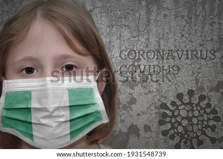 Little girl in medical mask with flag of nigeria stands near the old vintage wall with text coronavirus, covid, and virus picture. Stop virus
