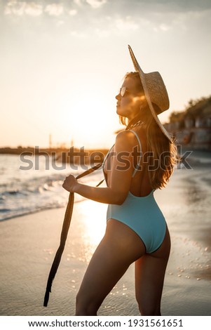 Young woman in a swimsuit and a hat on the seashore in the sunset light. Summer vacation concept. Selective focus