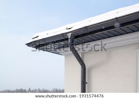 Corner of the house with new gray metal tile roof and rain gutter at winter. Metallic Guttering System, Guttering and Drainage Pipe Exterior Royalty-Free Stock Photo #1931574476