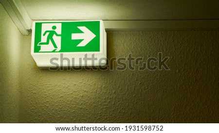 Green glowing emergency exit sign on wall in the house as a notice sign