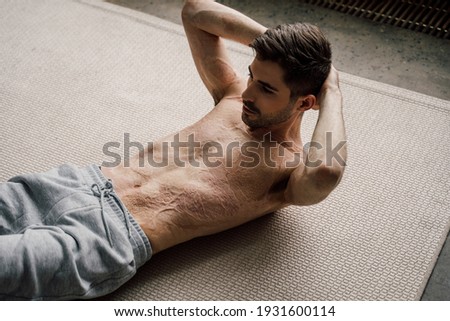 Sporty young attractive man with scars at the skin after burn practicing abdominal crunches, rock press exercise, working out, while training at home. Stock photo