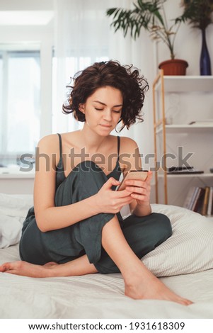 Portrait of focused dark-haired caucasian young woman staring at her smartphone screen in bed at the morning. Technology concept. Stock photo
