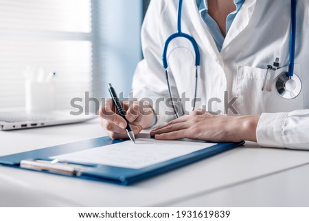Doctor sitting at desk and writing a prescription for her patient Royalty-Free Stock Photo #1931619839