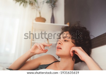 Cropped view of the cute young curly woman smoking  cannabis at the modern bedroom. Bad habits concept. Stock photo Royalty-Free Stock Photo #1931635619
