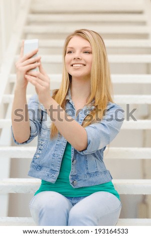 education and technology concept - smiling female student with smartphone sitting on staircase and taking picture