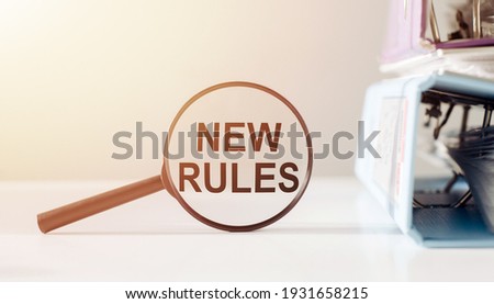 Magnifying glass with the word NEW RULES on office table.