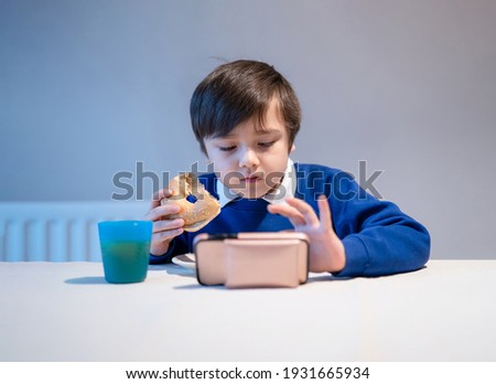 Kid eating whole grain bagels bagels for his breakfast,School boy watching cartoon mobile phone while eating donut healthy Child eating bread and juice drink for his breakfast.Healthy Children concept