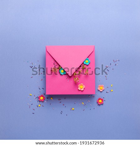Easter greeting card with cute handmade colorful eggs, kraft pink envelope and flowers on lilac background. Flat lay concept, top view with copy space.