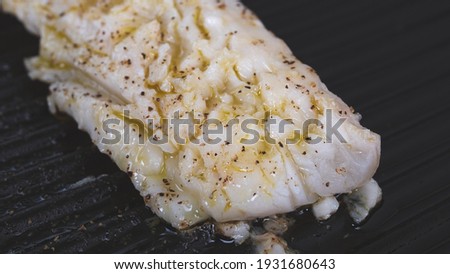 Flaky white cod fillet searing in a grill cast iron pan. Peppered gently and drizzled white olive oil and butter.