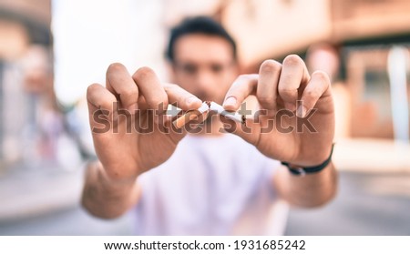 Young hispanic man breaking cigarette with hands walking at the city. Royalty-Free Stock Photo #1931685242