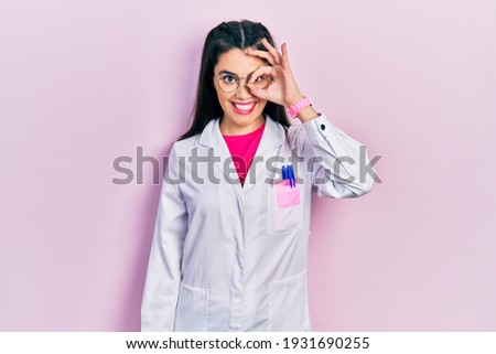 Young hispanic girl wearing scientist uniform smiling happy doing ok sign with hand on eye looking through fingers 