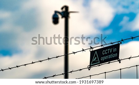 CCTV warning sign with camera in the background behind barbed wire