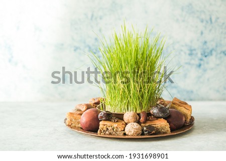 Novruz traditional tray with green wheat grass semeni or sabzi, sweets and dry fruits pakhlava on white background. Spring equinox, Azerbaijan copy space