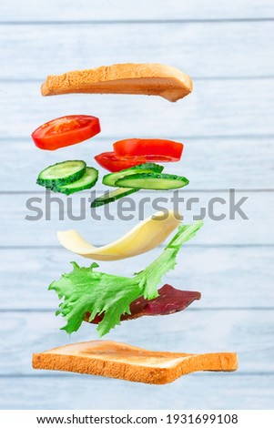 Flying layers of sandwich with ham, cheese, and vegetables on the wooden background. Breakfast food concept