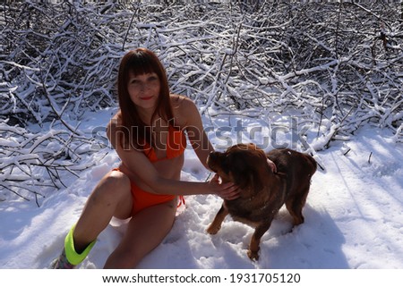 woman in orange swimsuit and her dog friend in the snow in winter