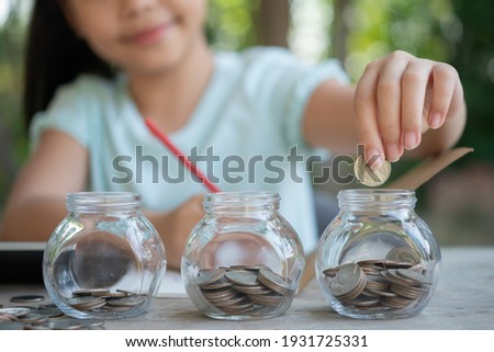 Cute asian little girl playing with coins making stacks of money,kid saving money into piggy bank, into glass jar. Child counting his saved coins, Children learning about for the future concept. Royalty-Free Stock Photo #1931725331