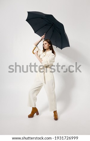 woman with an open umbrella over her head in a white suit posing in full growth