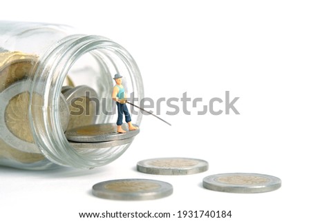 Miniature people toy photography. An angler standing above money jar fishing coin. Isolated on white background.