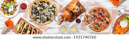 Healthy plant based fast food table scene. Overhead view on a white wood banner background. Cauliflower crust pizzas, bean burgers, mushroom tacos and vegetarian sides.
