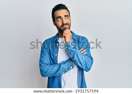 Young hispanic man wearing casual clothes thinking concentrated about doubt with finger on chin and looking up wondering  Royalty-Free Stock Photo #1931757194