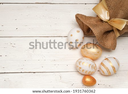 Golden Easter eggs in jute bag on rustic old wooden background. Trendy Easter flat lay composition. Copy space for text. Minimal Easter concept. Happy Easter day greeting card.                        