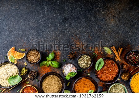 Set of Spices and herbs for cooking. Small bowls with colorful  seasonings and spices - basil, pepper, saffron, salt, paprika, turmeric. On black stone table top view copy space Royalty-Free Stock Photo #1931762159